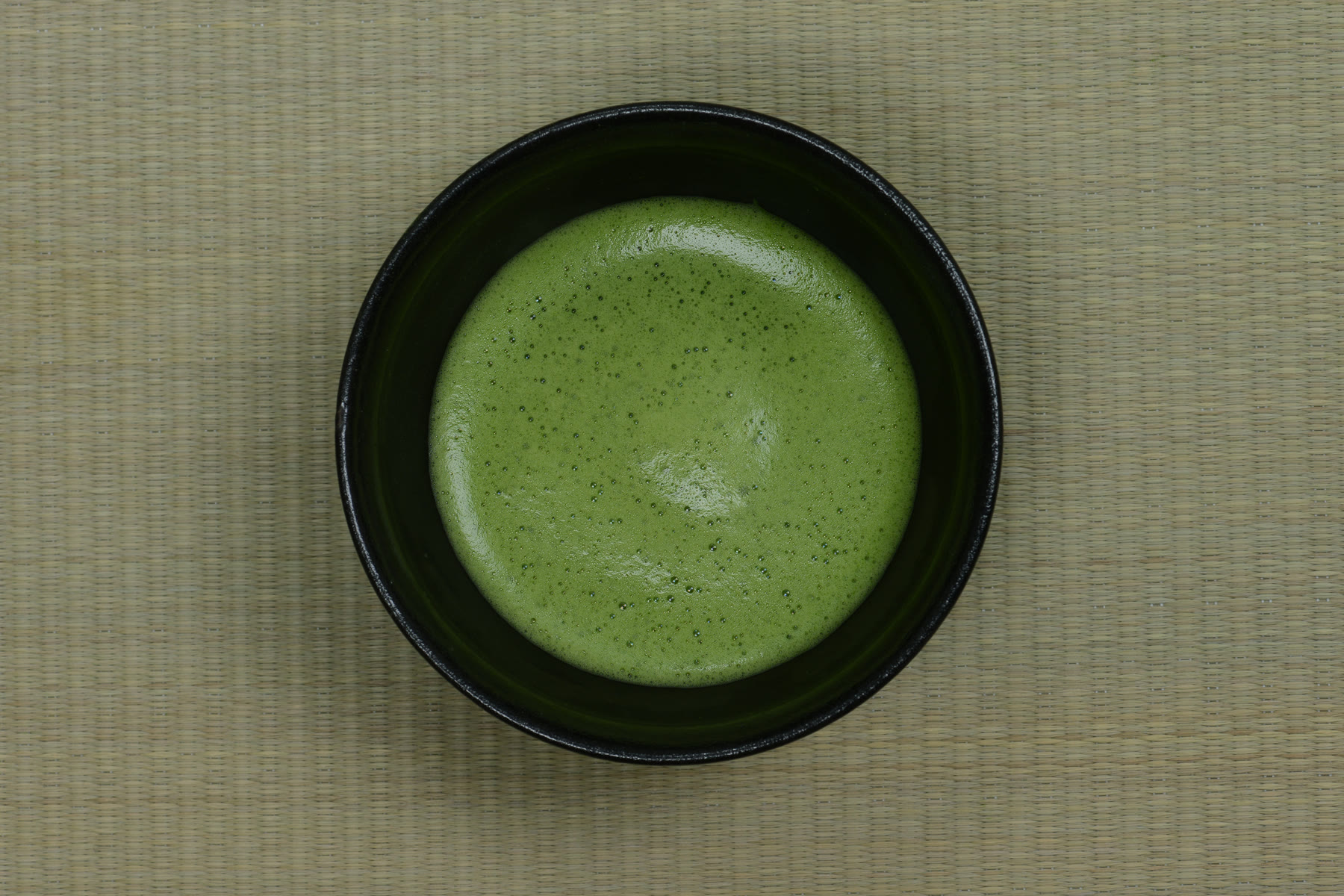 Matcha served in a black bowl on a woven mat