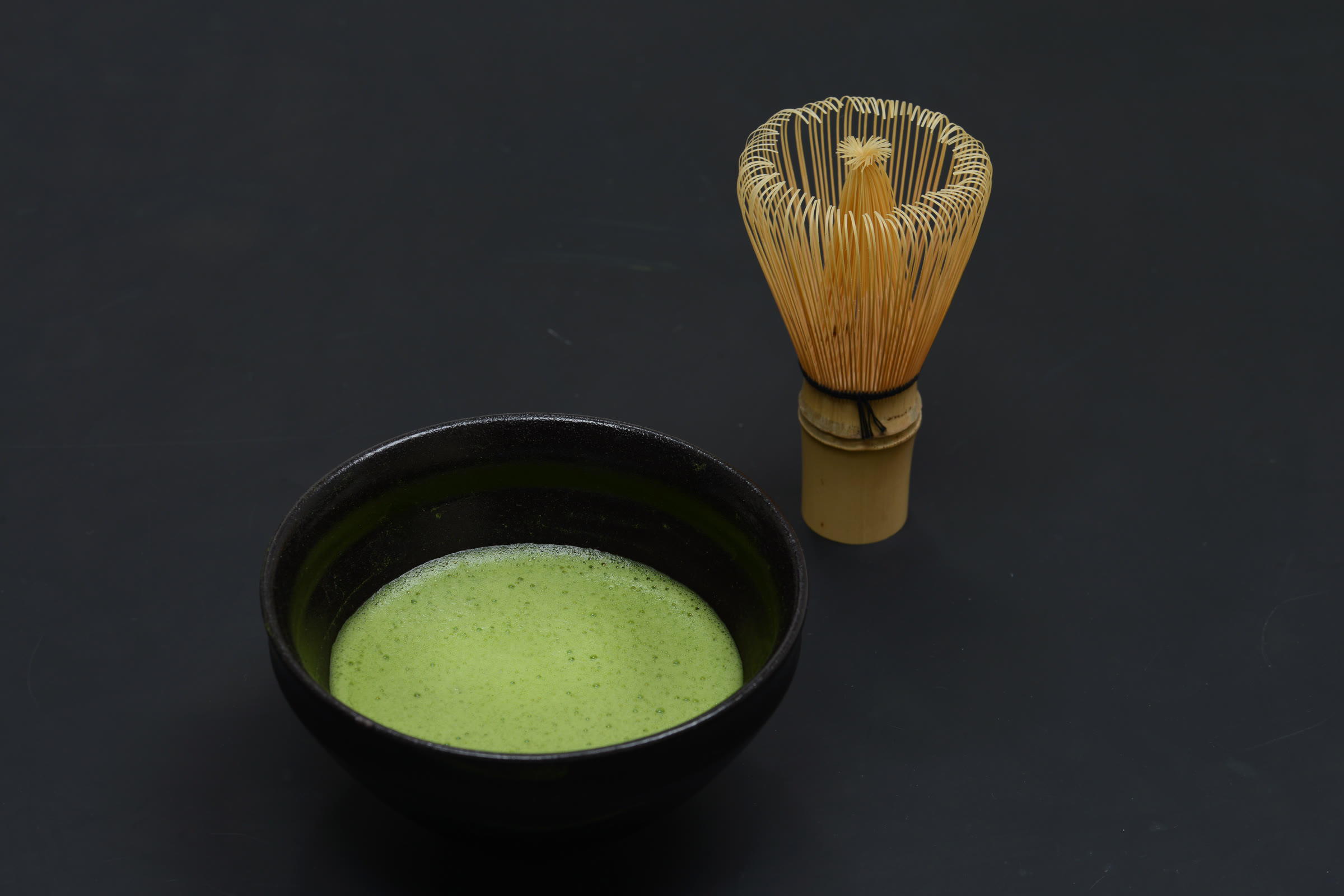 A prepared bowl of matcha beside a bamboo whisk